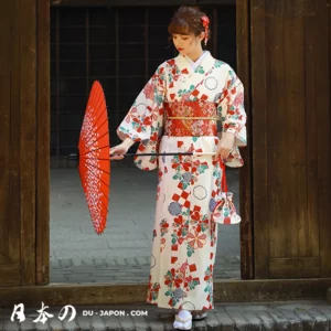 Jeune femme en kimono blanc fleuri, tenant un parasol rouge dans un cadre traditionnel.