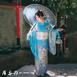 Femme en kimono bleu avec parasol floral dans un jardin paisible.