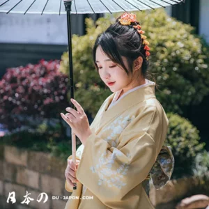 Femme en kimono jaune floral avec parasol dans un jardin paisible.