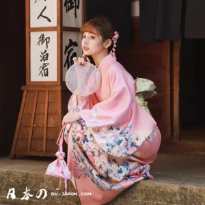 Femme en kimono rose avec ventilateur dans un décor traditionnel japonais.