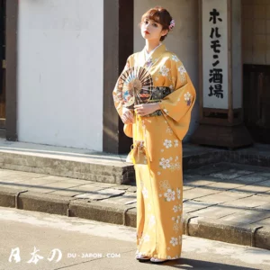 Femme en kimono jaune floral, élégante, avec éventail, dans un cadre traditionnel japonais.