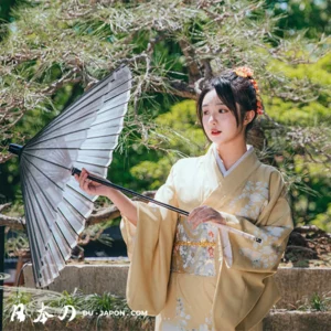 Femme en kimono jaune avec parasol dans un jardin zen japonais.