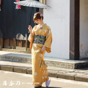 Femme en kimono jaune traditionnel marchant avec un parasol dans une rue japonaise.