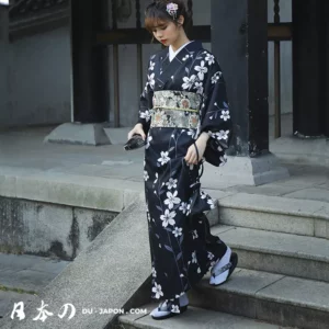 Femme en kimono noir floral marchant avec grâce dans un cadre traditionnel japonais.