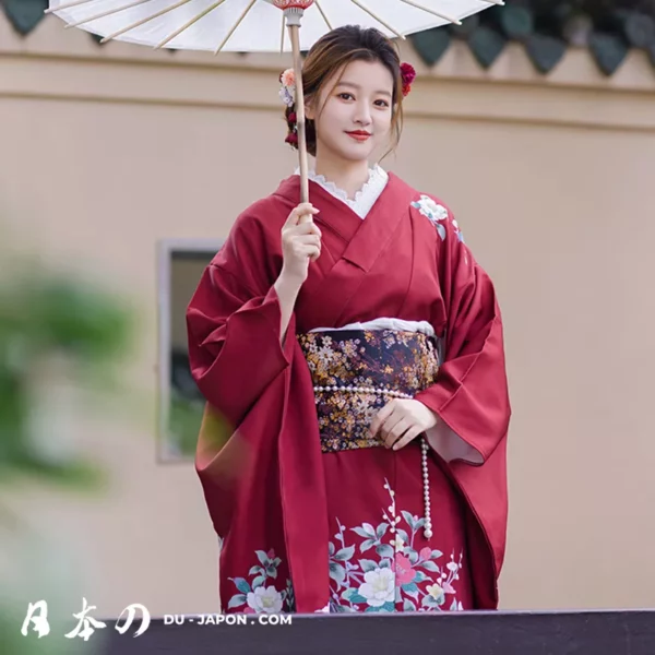 Femme en kimono rouge élégant dans un jardin fleuri, portant un parasol traditionnel.