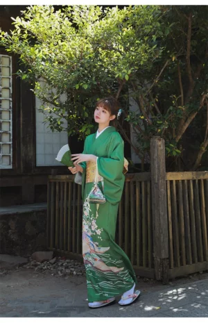 Femme en kimono vert traditionnel, fan à la main, dans un cadre naturel apaisant.