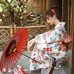 Femme en kimono coloré, parasol rouge, assise dans un cadre naturel japonais apaisant.