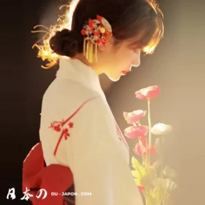 Femme en kimono blanc avec fleurs rouges, illuminée par une lumière douce et apaisante.