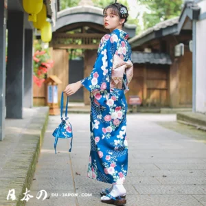 Femme en kimono bleu fleuri, souriante, dans un jardin japonais traditionnel avec geta.