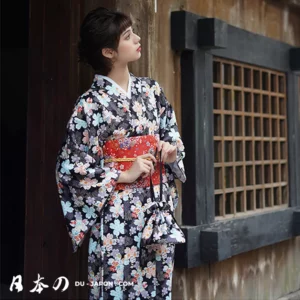 Femme en kimono floral avec obi rouge, devant un fond en bois traditionnel japonais.