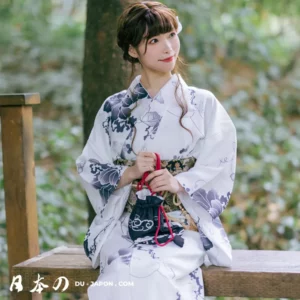 Femme souriante en kimono traditionnel blanc, assise dans la nature verdoyante.