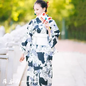 Femme en kimono à motifs de chats, souriante dans un jardin lors dun festival.