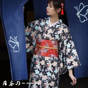 Femme en kimono floral avec obi rouge, devant un fond bleu et motifs de papillons.