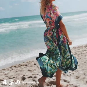 Femme en robe florale marchant sur une plage sereine, ciel bleu et vagues apaisantes.