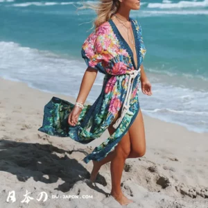 Femme en kimono floral marchant sur la plage, océan scintillant en arrière-plan.