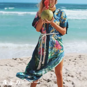 Femme en robe florale, dégustant un coco sur une plage ensoleillée et paisible.