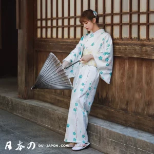 Femme en kimono blanc avec parasol, fleurs, dans un cadre historique japonais.