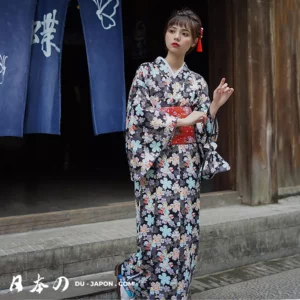 Jeune femme en kimono floral traditionnel devant un bâtiment japonais pittoresque.